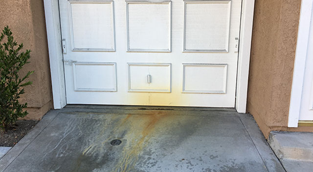 Results of an ongoing water leak in front of a garage that has stained the door and concrete over time.